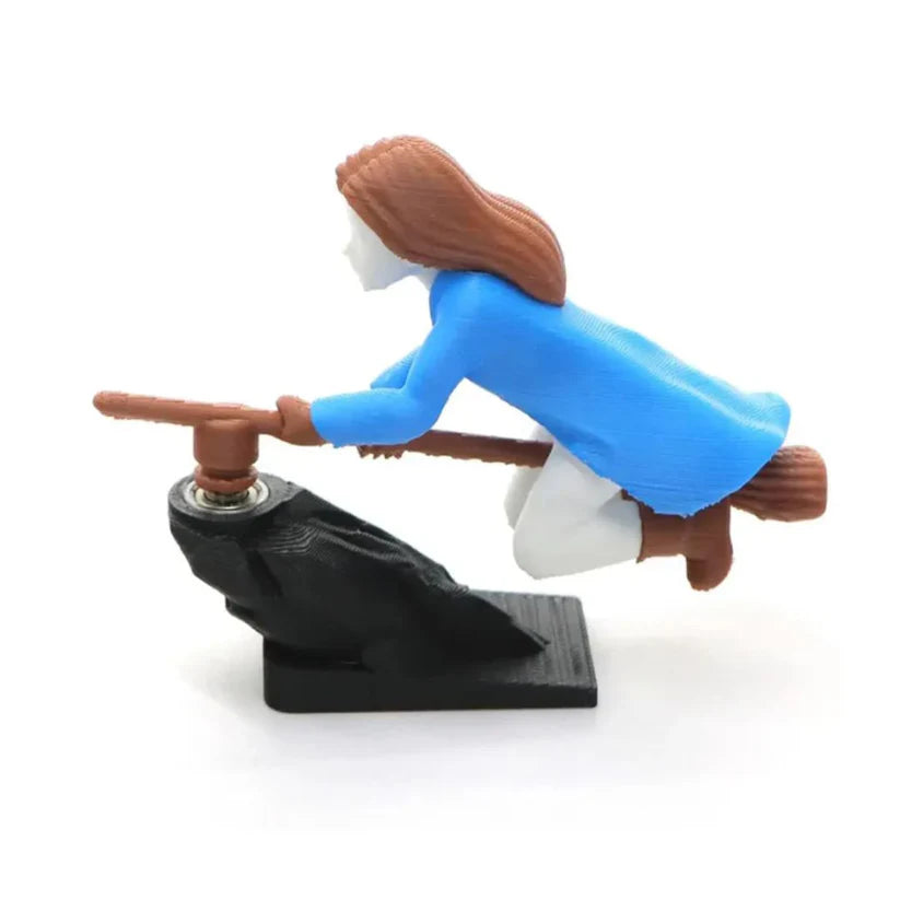 Profile view of a blue-coated witch riding a broomstick, designed as a drifting car ornament.