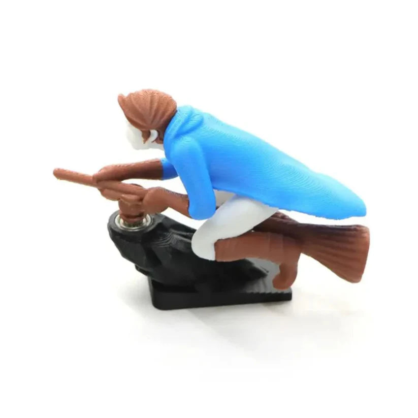 A blue wizard riding a flying broomstick car dashboard ornament, showing the motion-bearing mounting structure.