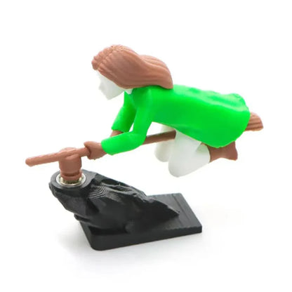 Side profile of a 3D-printed green witch riding a broomstick dashboard ornament on a black base.