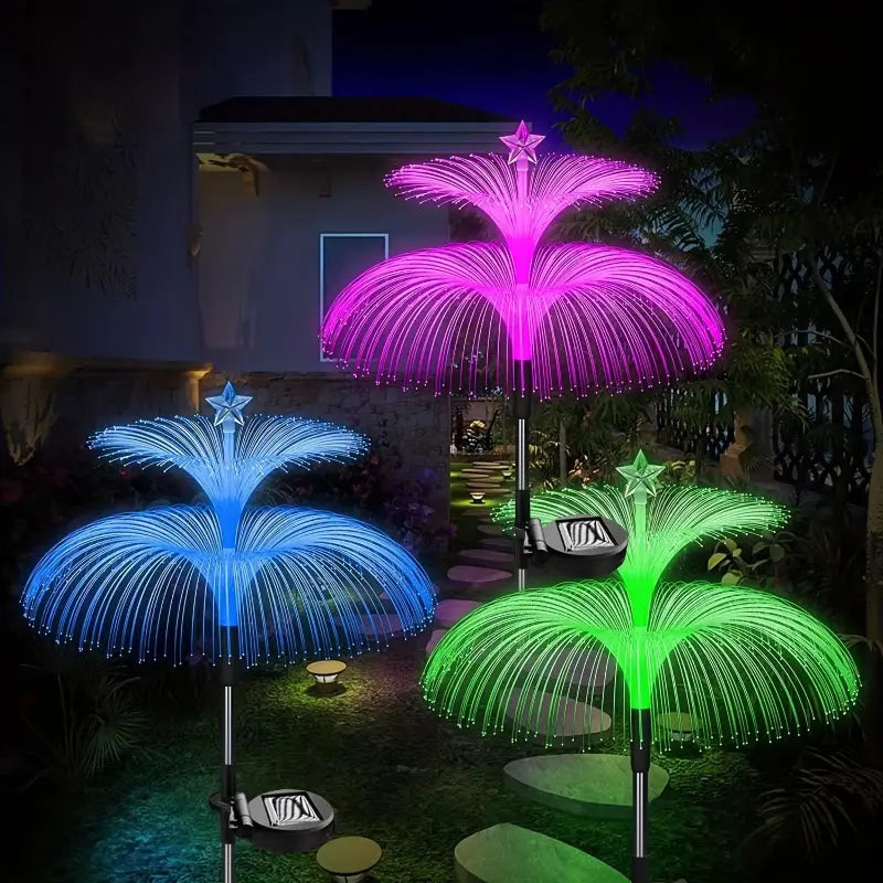 Three glowing dual-layer solar jellyfish lights in pink, blue, and green colors illuminating a garden path at night.
