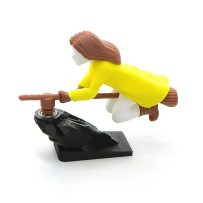Left profile view of a yellow-coated witch riding a flying broomstick car dashboard drift ornament.
